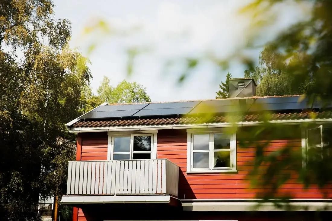 mindre rött hus med solceller på taket som producerar el i solsken
