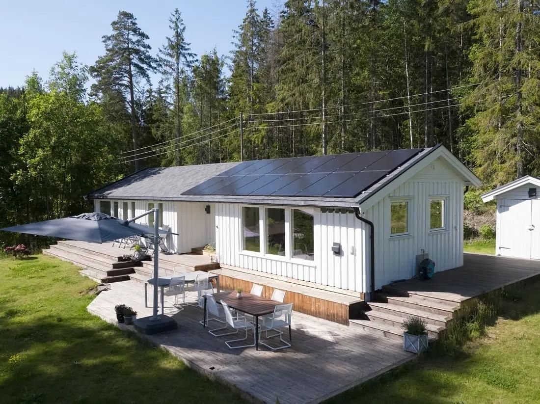 vitt enplanhus i skogsområde med terrass och solceller på taket