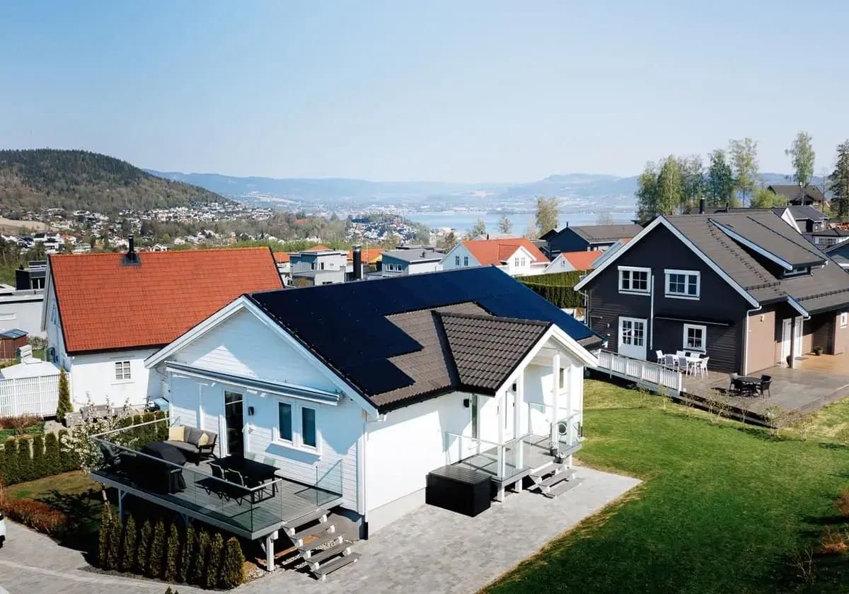 vit villa omgiven av hus i kuperat landskap med svarta solceller på taket