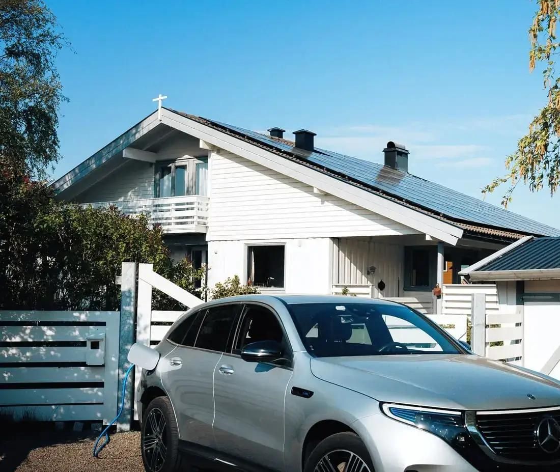 elbil på laddning på uppfarten framför ett vitt hus med solceller på taket